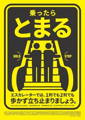 黄色の背景にエスカレーターのイラストが描かれた、マナー啓発ポスター。上部に「乗ったらとまる」、下部に「エスカレーターでは、1列でも2列でも歩かず立ち止まりましょう。」と大きく書かれている。イラストでは、2人の人物がエスカレーターのステップに並んで立ち、両側の手すりにつかまっている様子が描かれている。